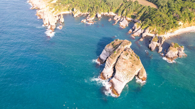 High angle aerial view of turquoise sea waves crashing against rocky shores and a green coastal forest in Kefken. - Powered by Adobe