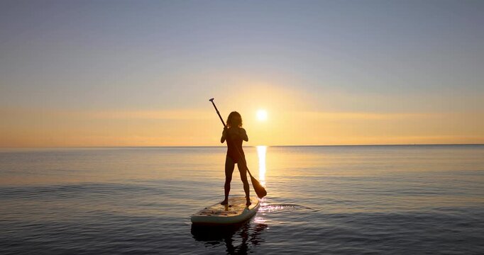 Young woman walking on stand up paddle sup boards by the sea during summer vacation. Beautiful girl flat water paddling against sea and sky background