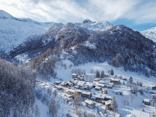 Aerial view of a snow-covered village nestled amidst towering mountains, their peaks dusted with glistening snow, Balme, Piedmont, Italy.