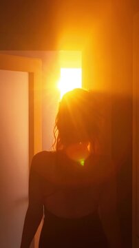 shadow black silhouette of young woman in long dress, walks through house long dark corridor, magical light at end room sunset sun rays from window. Door is open. Adult sexy girl. vertical video crop
