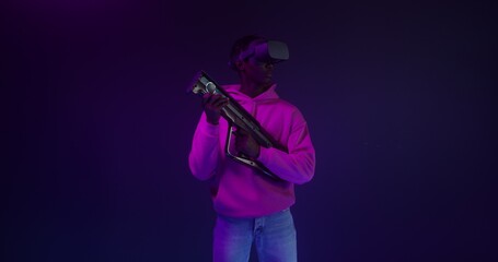 Obraz premium A man in virtual reality glasses with a game gun in his hands in a VR studio