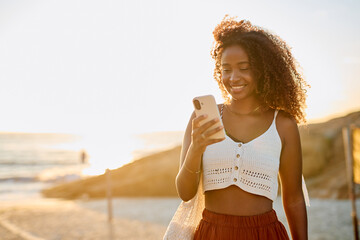Woman enjoying a beach vacation, messaging on her mobile phone during golden hour. Leisure travel...