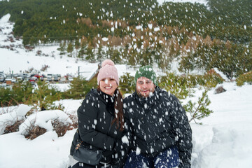 Young couple enjoying winter snowfall in mountain forest