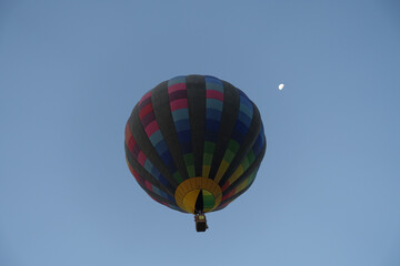 Hot air balloon flying before dawn against the moon and early dawn sky