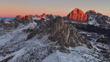 Aerial view of a winter sunrise on Giau Pass in Italian Dolomites.Snow covered mountain road. Majestic alpine peaks and warm morning light. Cinque Torri in the Dolomites. Sunrise in winter dolomites