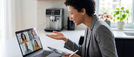 Professional woman speaks in a hybrid meeting setup with remote colleagues on screen, showing flexible and modern business communication.