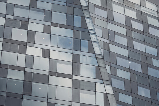 Modern urban architecture facade shows glass windows on a building with grid pattern and reflection across faceted office surfaces
