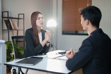 Woman and man in professional dress discuss recruitment and candidate evaluation during a serious business meeting in a corporate office, reviewing applicants and hiring decisions