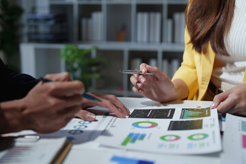Business professionals reviewing financial documents and charts, collaborating on a project, and discussing market trends during a corporate meeting in an office environment
