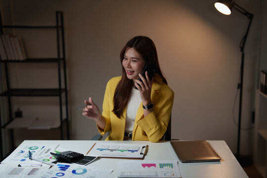 Young businesswoman on a late-night call reviewing financial charts and reports at her desk, focused on strategy, analysis and planning to meet deadlines and drive growth - Powered by Adobe