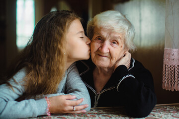 Young girl kissing an elderly woman on the cheek indoors, showing family affection and care, with soft natural light and a warm, intimate atmosphere.