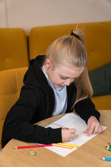 Young girl focused on drawing with colored pencils at a desk, developing creativity and skills while enjoying a quiet home art activity and playful learning moment. Vertical photo