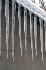 Icicles hanging from the edge of a roof in winter with snow on the ground and cold weather conditions