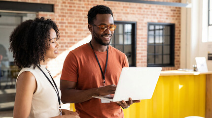 Two young professionals standing together and looking at laptop screen in office