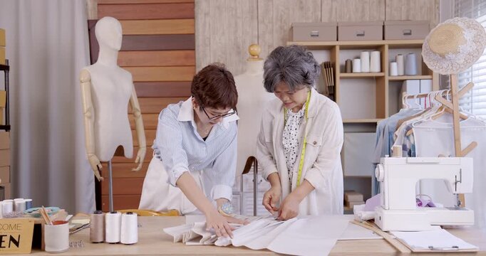 Senior asian woman and daughter carefully folding fabric pleats boutique fashion studio teamwork sewing handmade textile family business designer apparel pattern making garment clothing