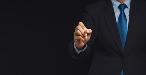 Confident businessman pointing forward on dark background.