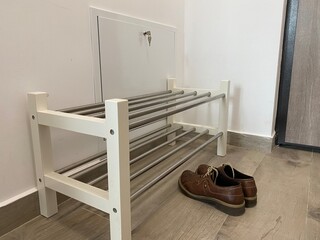 Shoe rack with multiple metal rods, featuring brown leather shoes placed beside it, set in a modern entryway with minimalist design elements and neutral color tones