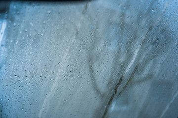 Raindrops on a car glass window with a blurred green background. Close up shot, shallow depth of field, no people