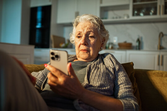 Concerned senior woman reading smartphone at home