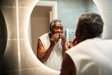 Senior man grooming face in bathroom mirror