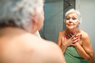 Senior woman with undereye patches looking in bathroom mirror