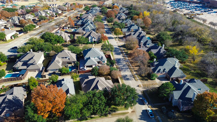 Coppell homes arranged along parallel streets with pools, fences, and fall trees; upper corner shows a full parking lot beside leafless woods, blending residential and natural zones, Texas