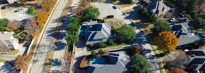 Panorama aerial view Coppell homes with pools and curved yards surround vertical main road; autumn trees and cul-de-sacs add rhythm to clean residential layout and seasonal vegetation, Texas