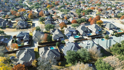 Coppell homes arranged in a curved grid with fenced yards, pools, and landscaped lawns; fall trees scattered throughout add warmth to the structured suburban layout and spacing, Texas
