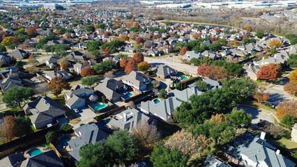 Coppell homes with pools and fall trees arranged in a curved grid with cul-de-sacs; mixed roof colors and distant commercial buildings show residential density near urban, suburbs Dallas, Texas