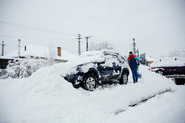 Man removes snow near car on a winter morning, outside his home in a residential area