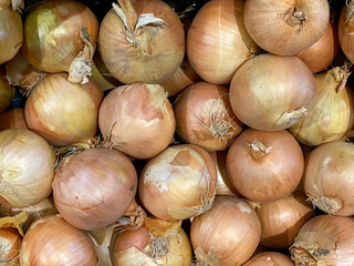 Pile of fresh yellow onions with papery skins and dried roots at market stall. Top view.