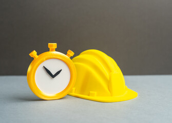 A stopwatch and a yellow construction hard hat. Temporary part-time work, seasonal work. Overtime. Flexible labor, time tracking and workforce intensity in construction.