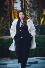 A beautiful middle-aged businesswoman in a business suit and white coat walks down the street. Vertical photo.