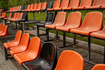 Naklejka premium Close up of Rows of empty orange and black plastic seats on grandstand near outdoor sports stadium