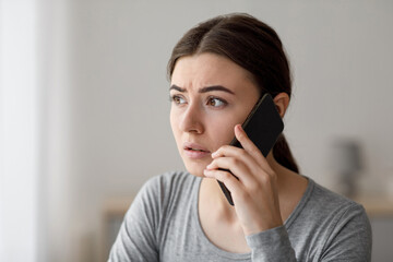 Portrait of worried anxious upset millennial lady talks by phone, received bad news at home, close up, free space. Depressed facial expression, stress, problems at work, trouble and panic indoor