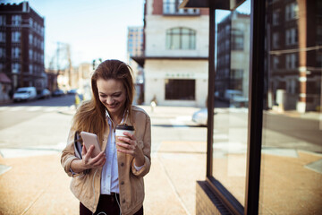 Young woman using smartphone with coffee on city street