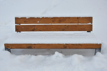 brown-orange snow covered wooden bench  standing in snow outdoors in winter yard.