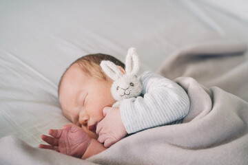 Newborn sleep at first days of life. Portrait of new born baby one week old with cute soft toy in crib in cloth background.