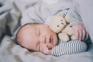 Newborn sleep at first days of life. Portrait of new born baby one week old with cute soft toy in crib in cloth background.