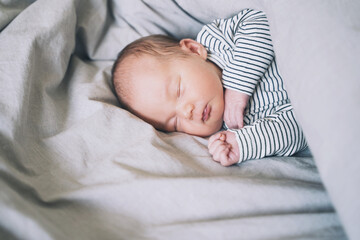 Newborn sleep at first days of life. Portrait of new born baby one week old in crib in cloth background.
