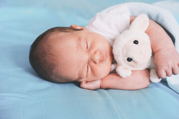 Newborn sleep at first days of life. Portrait of new born baby one week old with cute soft toy in crib in cloth background.