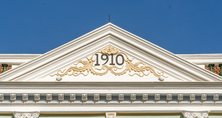 Historic architectural facade in Singapore featuring a triangular pediment inscribed with the year 1910, surrounded by gold embellishments.