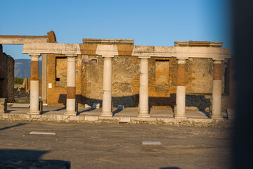 Fototapeta premium Ancient marble columns and brick entablature are illuminated by warm evening light in the civil forum of Pompeii, Italy. The textured stonework and faded inscriptions stand out against the open plaza