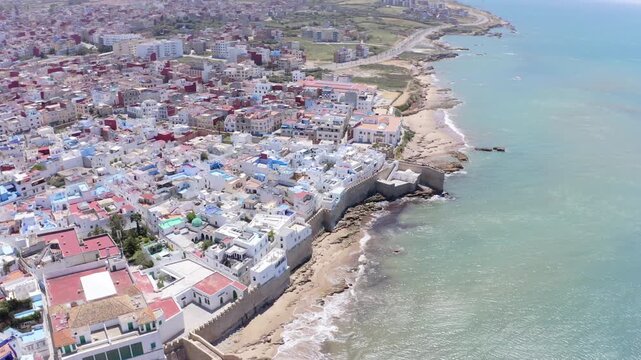 Assilah, Morocco - May 8, 2024: Wide orbit drone shot of Assilah, Morocco, featuring the historic city surrounded by ancient walls, overlooking the Atlantic Ocean with mountains in the background, hig