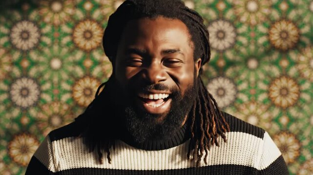 Laughing man with dreadlocks in front of patterned wall