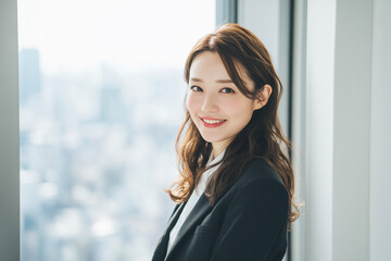 オフィスの窓際に立つカメラ目線の若い日本人女性のポートレート