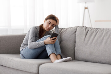 Sad depressed worried european millennial woman sitting on couch receiving bad news, waiting for...