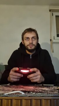 Vertical shot of a focused man in his Swiss living room, playing video games intensely, talking to himself, with fast-moving fingers and eyes illuminated by the glowing screen