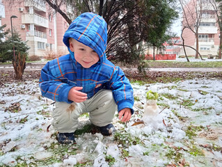 A boy kneels on the ground in a residential area covered in snow and ice. He smiles while making a...