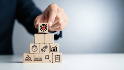 Business Strategy and Goal Setting: Hand Placing Target Icon Wooden Block on Stack of Cubes Representing Analytics, Planning, and Process Optimization on Clean Background
